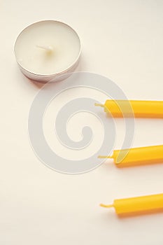Low white and three yellow candles on white table