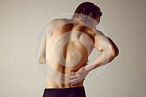 Lower back pains. Rear view of shirtless young man suffering from back pains against grey studio background