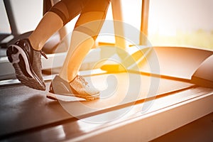 Lower body at legs part of Fitness girl running on running machine or treadmill in fitness gym with sun ray. Warm tone. Healthy