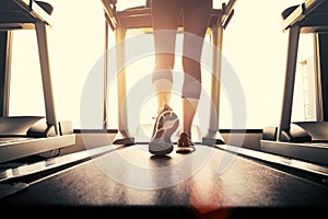 Lower body at legs part of Fitness girl running on running machine or treadmill in fitness gym with sun ray. Warm tone. Healthy