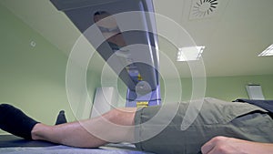 Lower body of a male patient is getting analyzed by a x-ray machine.