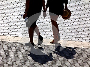 Lower body of young couple in silhouette shape in bright light walking on cobblestone pavement in urban setting