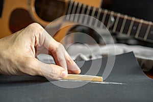 Lower the height of an acoustic guitar saddle for a better playability by sanding down a bone saddle with sandpaper