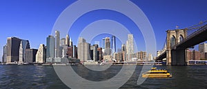 Lower Manhattan skyline, Eastern River and Brooklyn Bridge with a yellow water taxi boat on the foreground, New York City