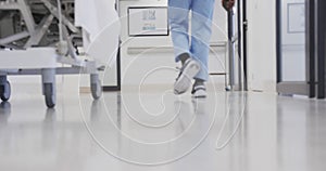 Lowsection of african american male doctor with smartphone walking in hospital corridor, slow motion