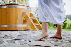 Lowsection of woman in bathrobe standing barefoot in terrace with hot tub, enjoy walking without slippers.