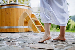 Lowsection of woman in bathrobe standing barefoot in terrace with hot tub, enjoy walking without slippers. photo
