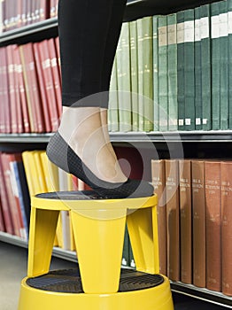 Lowsection Of Woman On Stool Reaching For Book