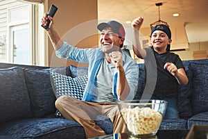 Loyal supporters of their favourite sports team. an enthusiastic father and son watching a sports match on tv at home.
