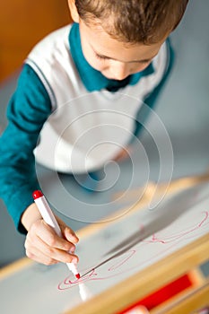 Lttle boy drawing on white board with felt pen and smiling