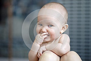 Lttle cheerful baby without shirt. Happy smiling child leaning on mothers kneels with fingers in mouth. Love, tenderness