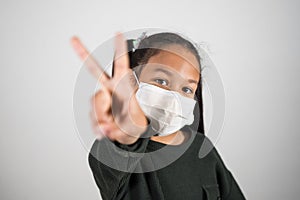 Lttle girl with medical mask show v sign with hand, healthcare and infection control. Concept of positivism against the infection photo