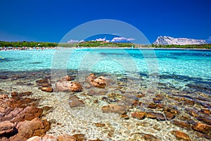 Lu Impostu beach with Isola Travolara in the background, red stones and azure clear water, Sardinia, Italy