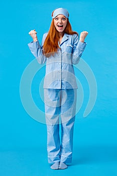 Luck, happiness and victory concept. Vertical full-length studio shot cheerful triumphing redhead female in nightwear