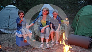 Lucky family weekend in forest, mother and two children sitting around on straw bale beside balefire, mom and kids