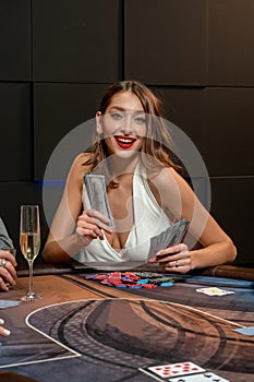 Lucky girl sitting at poker table in casino with fan of banknotes