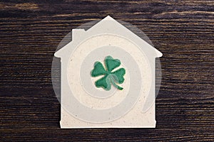 Lucky home symbol with four-leaf clover on wooden background.