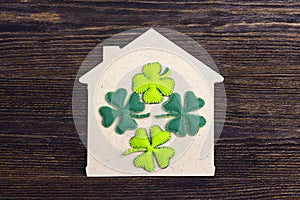 Lucky home symbol with four-leaf clover on wooden background.