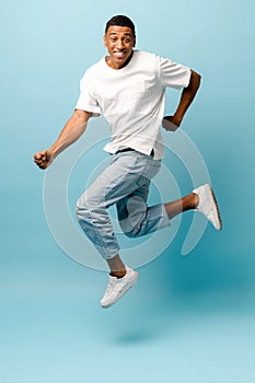 Lucky joyful African-American young guy jumping on blue background