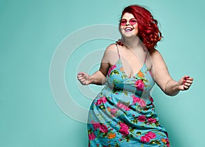 Lucky plus-size lady overweight woman in fashion sunglasses and colorful sundress happy dancing, celebrating