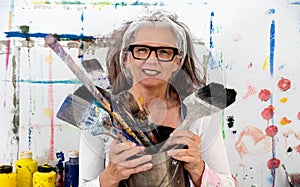 Lucky, proud portrait of an older mature smiling woman, artist, in her fifties with grey hair and glasses, and many big