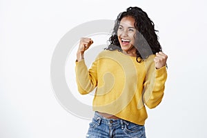 Lucky venturous young african-american girl fan in yellow sweater, making fist pump gesture as smiling and looking left photo