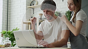 Lucky Winners. Excited couple with laptop in kitchen celebrating success