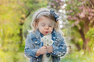 lue-eyed little blond girl blowing dandelion outdoors