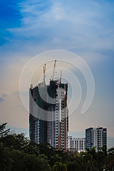 Luffing jib tower cranes on the top of under construction building with sunset sky background. Silhouette of the building