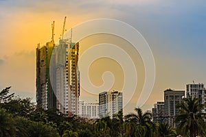 Luffing jib tower cranes on the top of under construction building with sunset sky background. Silhouette of the building