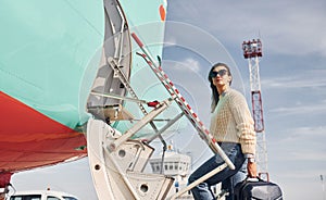 With lugagge. Young female passanger in casual clothes is outdoors near the plane photo