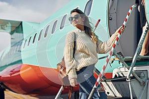 With lugagge. Young female passanger in casual clothes is outdoors near the plane photo