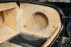 Luggage compartment of a black car sedan with a box made of wood and sawn holes for the installation of subwoofers and speakers