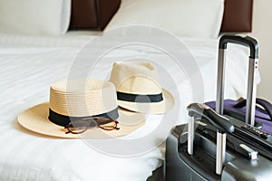 Luggage and hat of a couple on bed in modern hotel room with windows, curtains. Travel, relaxation, journey, trip and vacation