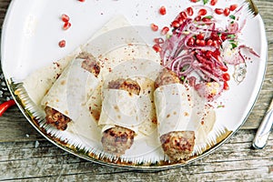 Lula kebab in lavash with pomegranate and onion on a plate