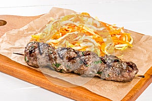 Lula kebab with vegetables on a wooden board and white background