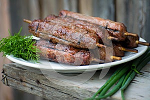 Lulya kebab from meat on a white plate and wooden board with dill and green onions.