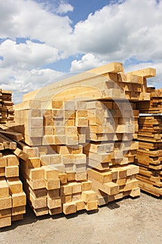 Lumber warehouse in the open air. Wooden beam, planks of wood, stacked in stacks. Sunny day, blue sky with clouds