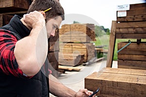 Lumber yard worker, carpenter at wood yard counts inventory with mobile device