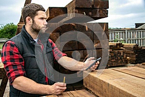 Lumber yard worker, carpenter at wood yard counts inventory with mobile device