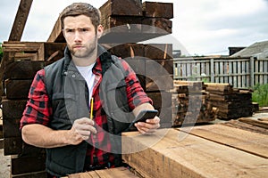 Lumber yard worker, carpenter at wood yard counts inventory with mobile device