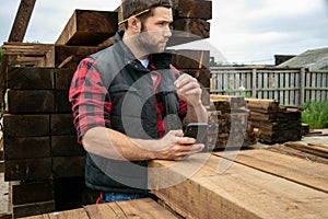 Lumber yard worker, carpenter at wood yard counts inventory with mobile device