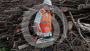 Lumberjack with chainsaw at the pile of branches