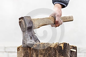 Lumberjack holds the handle of a sharp ax hammered in old stump.