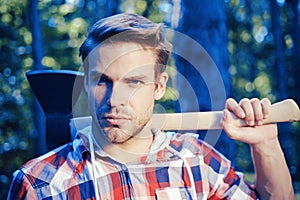 Lumberjack man carries axe on shoulder. Woodcutter with axe in the summer forest. Lumberjack holding the axe.