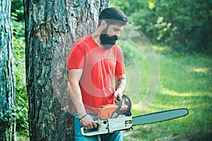 Lumberjack in the woods with chainsaw axe. Handsome young man with axe near forest. Lumberjack with chainsaw on forest