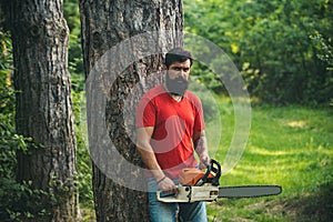 Lumberjack worker with chainsaw in the forest. Handsome young man with axe near forest. Stylish young man posing like