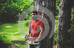 Lumberjack worker with chainsaw in the forest. Handsome young man with axe near forest. Stylish young man posing like