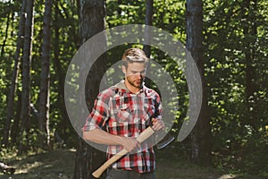 The Lumberjack working in a forest. Handsome young man with axe near forest. Woodcutter with axe in the summer forest