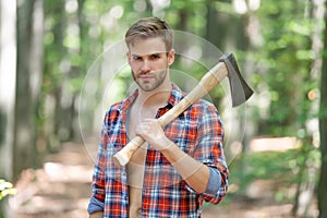 Lumbersexual man in lumberjack shirt holding axe on shoulder forest background photo